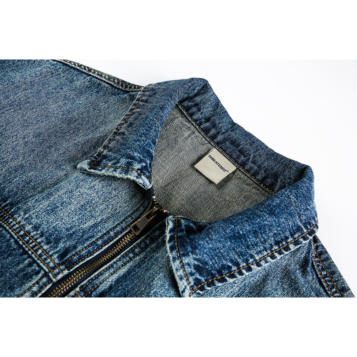 Close-up of a blue denim jacket collar, zipper, and inner neck label.