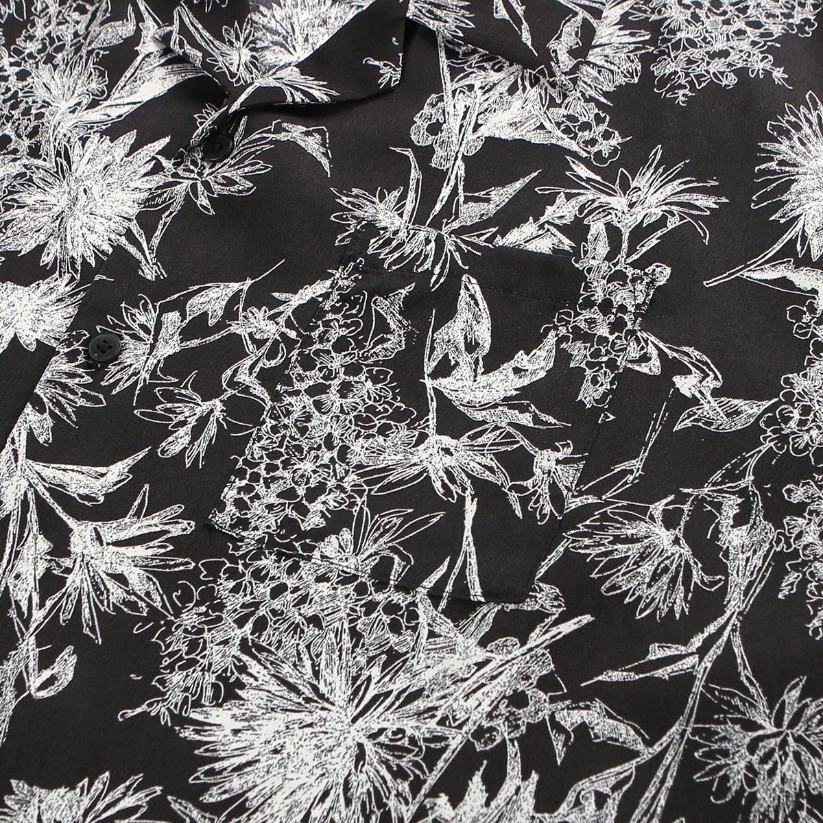 Close-up of the black shirt's white botanical print, collar, dark buttons and chest pocket.