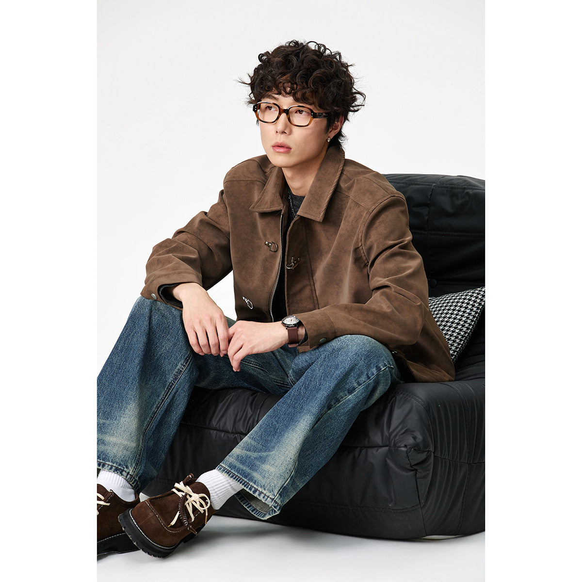 Seated model wearing a brown collared jacket with metal toggle closures and blue jeans.