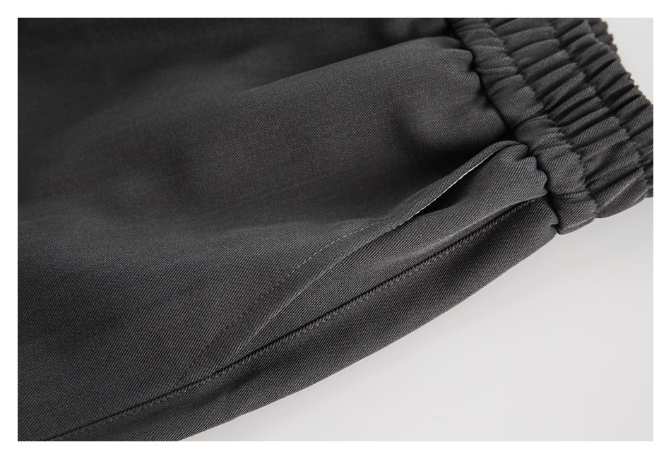 Close-up of a side pocket opening and gathered waistband on charcoal gray pants.