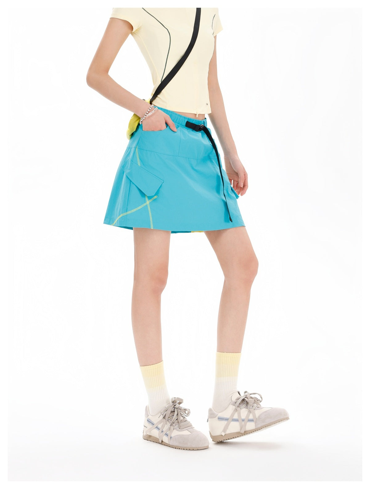 Model wearing a turquoise flared skirt with lime accents, a black belt, and a flap pocket, paired with a cream top.