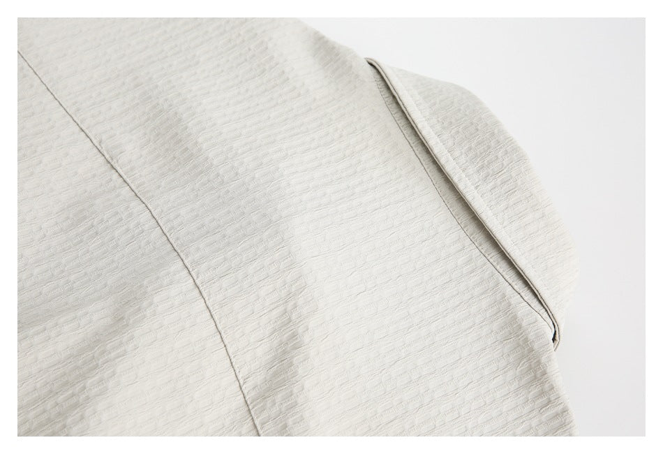 Close-up of ivory garment fabric with a curved folded edge and stitched seam.