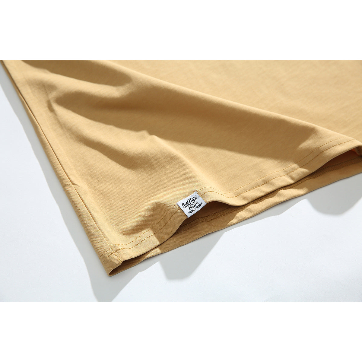 Close-up of the tan sleeveless shirt's stitched hem and small sewn label.