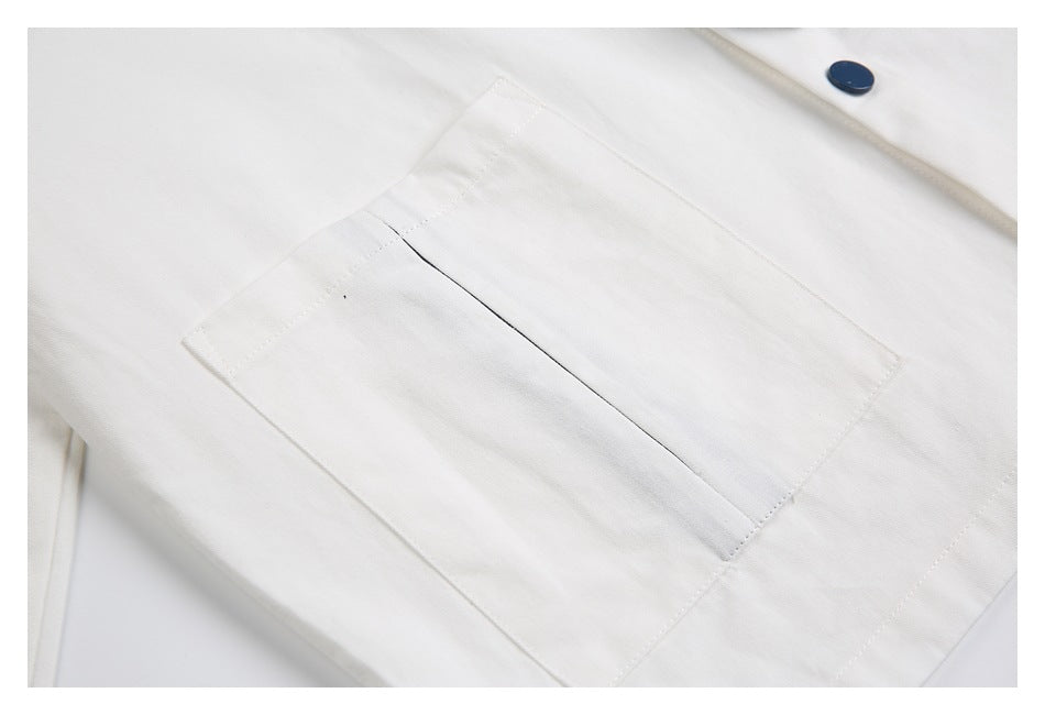 Close-up of a rectangular patch pocket on a white garment, with a dark blue button nearby.