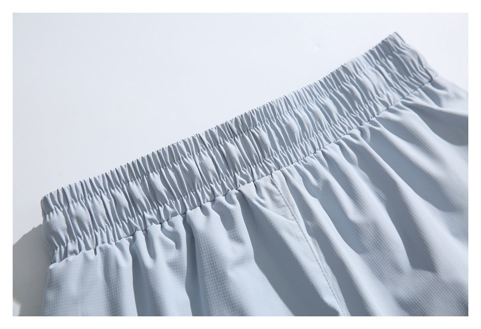 Close-up of the gathered elastic waistband and stitched center seam on pale blue-gray shorts.