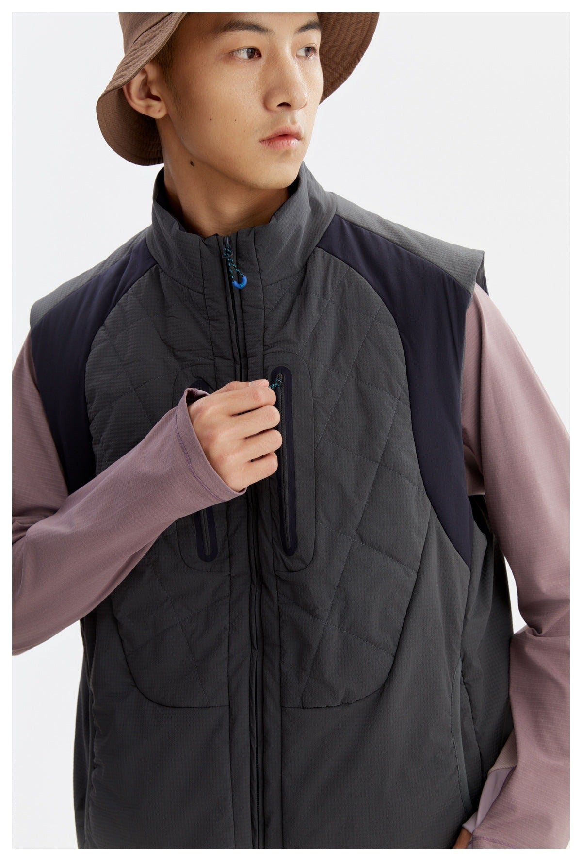 Close-up of a charcoal quilted vest showing its high collar, blue zipper pull, and vertical zip chest pockets.