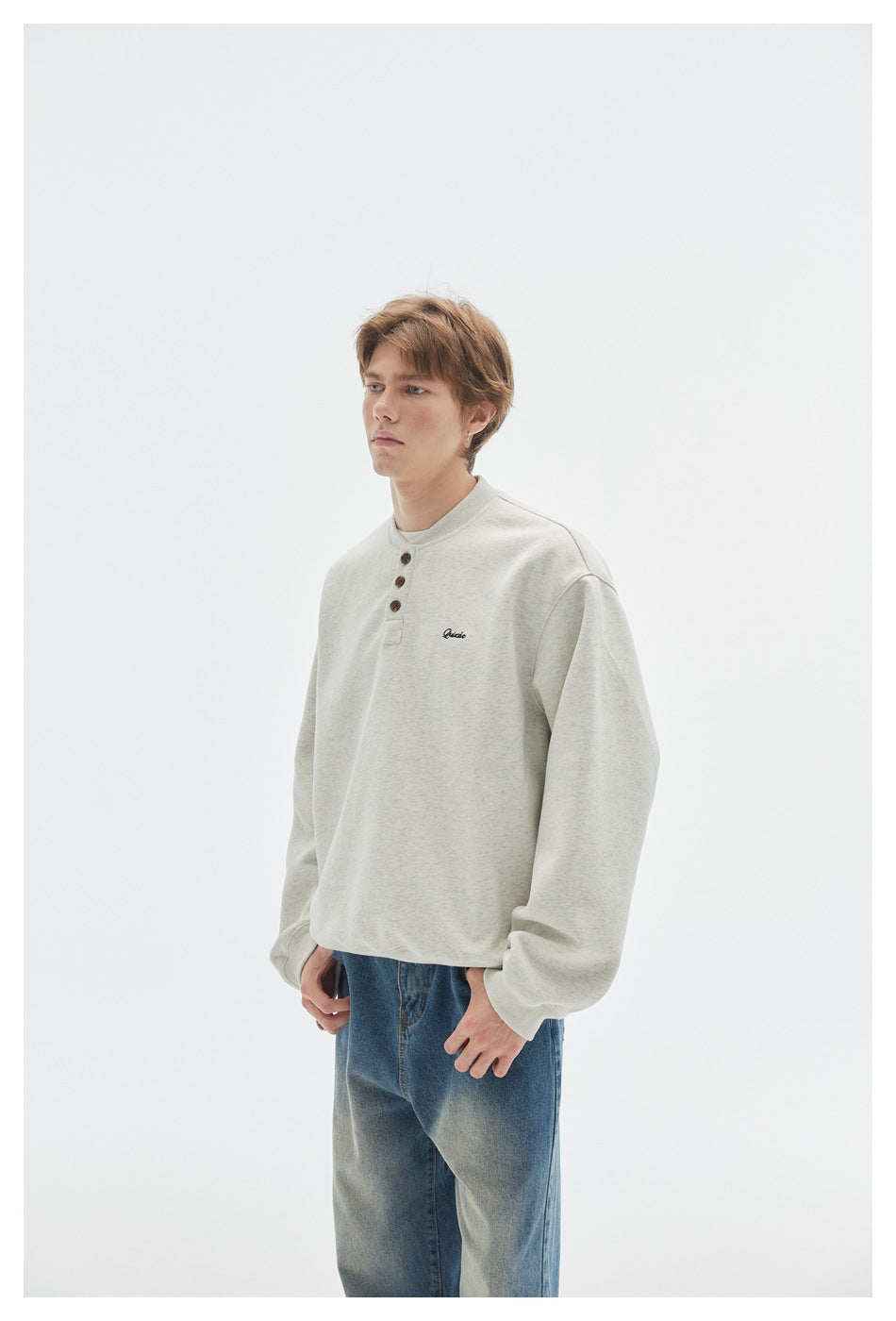 Model wearing an off-white henley sweatshirt with three buttons and small chest embroidery, paired with blue jeans.