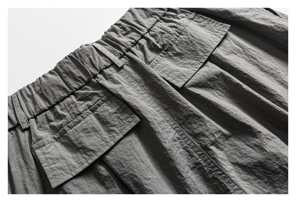Close-up of a charcoal gray garment with a gathered waistband, stitched belt loops, and a large patch pocket.