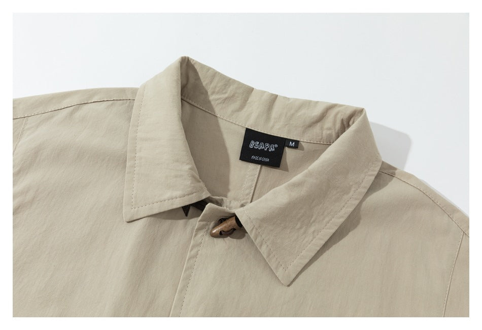 Close-up of a beige collared jacket showing its brown toggle closure and black neck label.