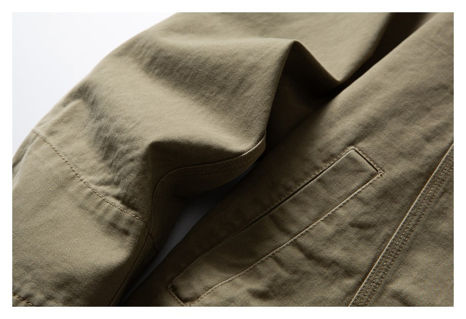 Close-up of an olive-khaki garment with a folded flap and stitched rectangular pocket.