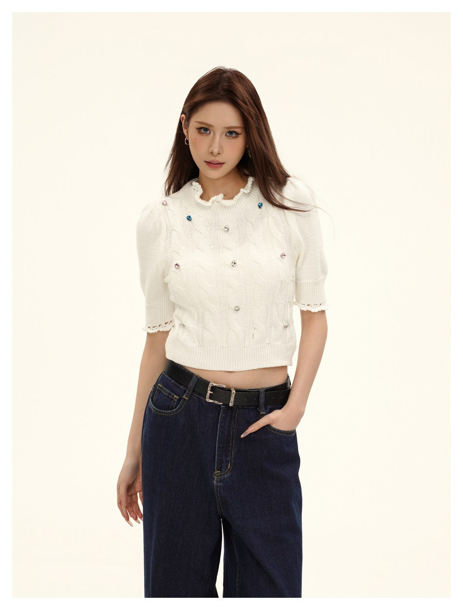 Close-up of a model in a cream cable-knit puff-sleeve top with ruffled collar and multicolor gems, with dark jeans