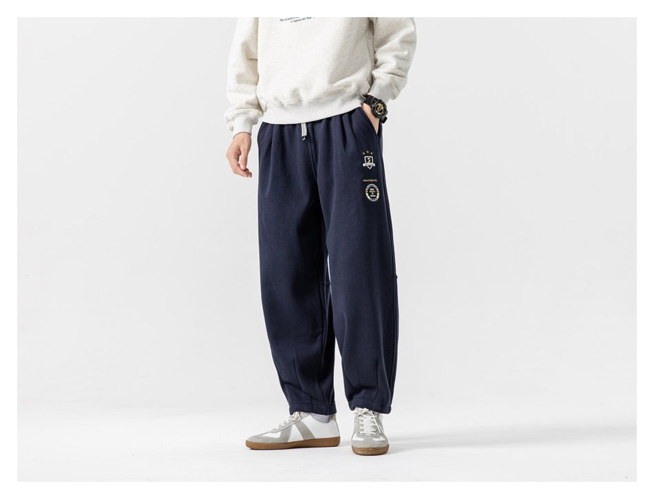 Front view of a model wearing loose navy joggers with a drawstring waist, ankle cuffs and small embroidered leg graphics.