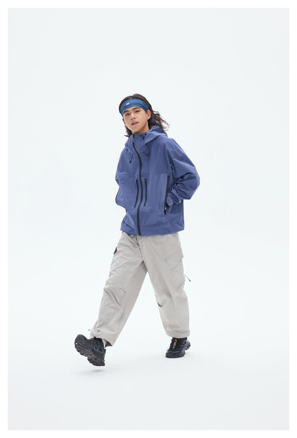 Model in a blue hooded jacket and light gray cargo pants, stepping forward against a white background.