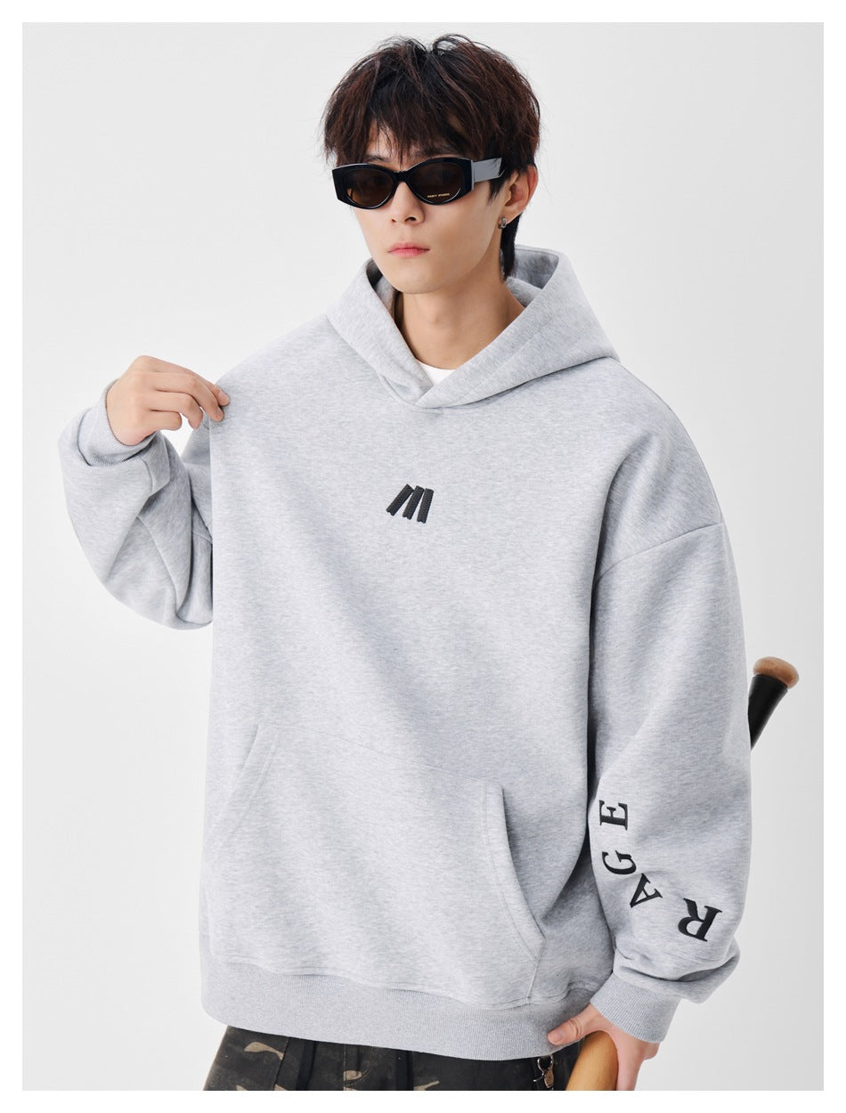 Close view of a light gray hoodie on a model, showing its black chest mark, kangaroo pocket, and sleeve lettering.