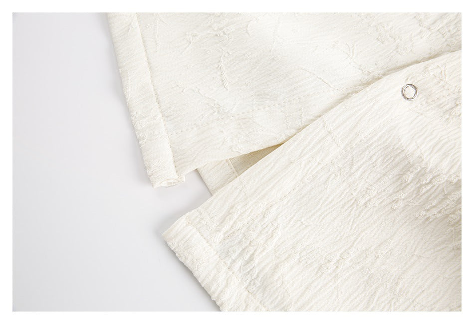 Close-up of ivory textured garment fabric with a small metal eyelet and overlapping panels.