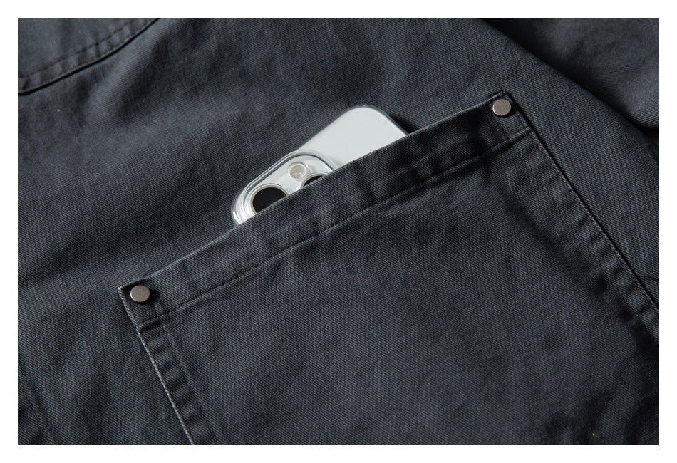 Close-up of a dark charcoal jacket pocket with metal rivets and a smartphone tucked inside.