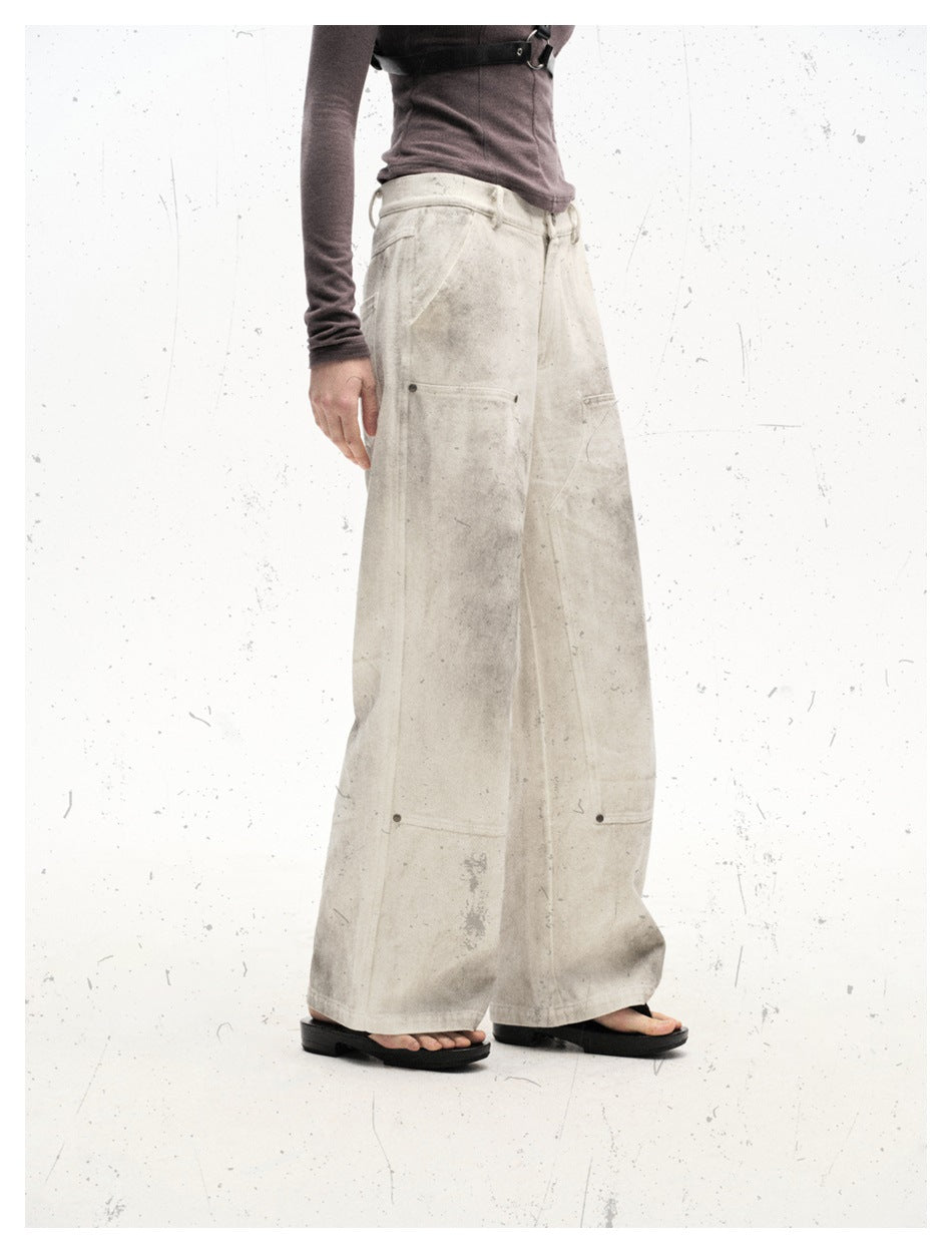 Side view of a model wearing very wide-leg off-white trousers with gray distressed marks and large panel pockets.