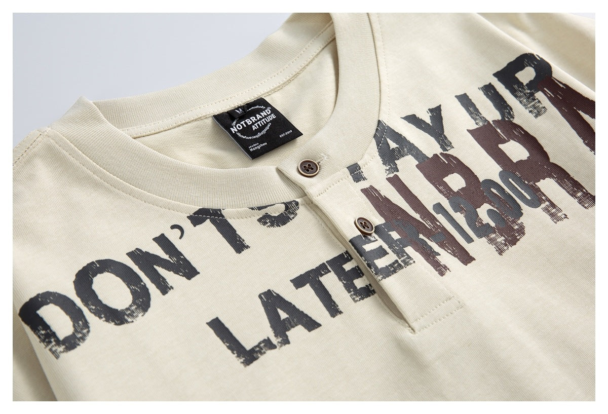 Close-up of an ivory Henley shirt with a two-button placket and distressed dark lettering across the chest.