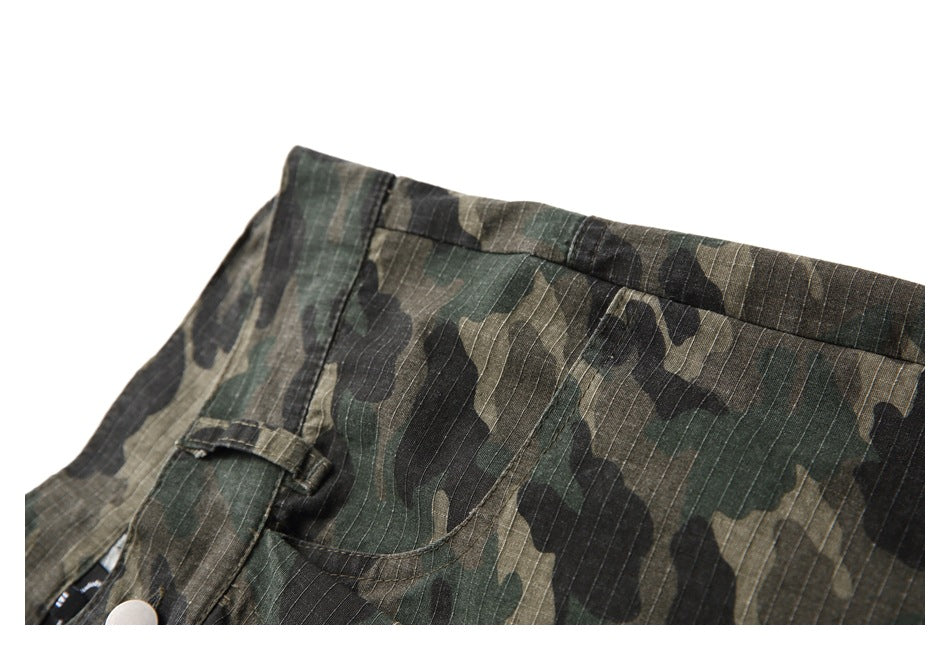Close-up of a curved front pocket and waistband on olive and black camouflage trousers.