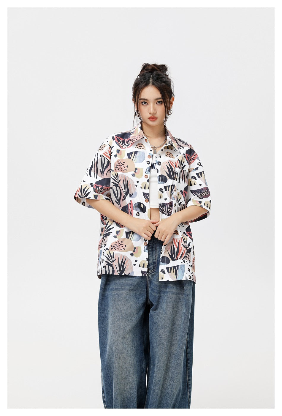 Model wearing open white botanical-print short-sleeve shirt over a white top with wide-leg jeans, 3/4 view