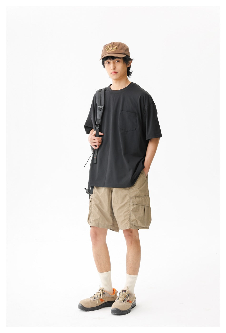 Front view of a model wearing a black pocket T-shirt and tan cargo shorts.