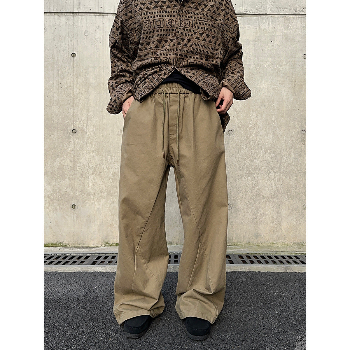 Model wearing loose tan drawstring trousers with a brown geometric-patterned top.