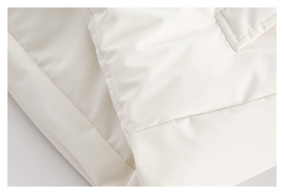 Close-up of off-white garment fabric with stitched panel seams and a small folded corner detail.
