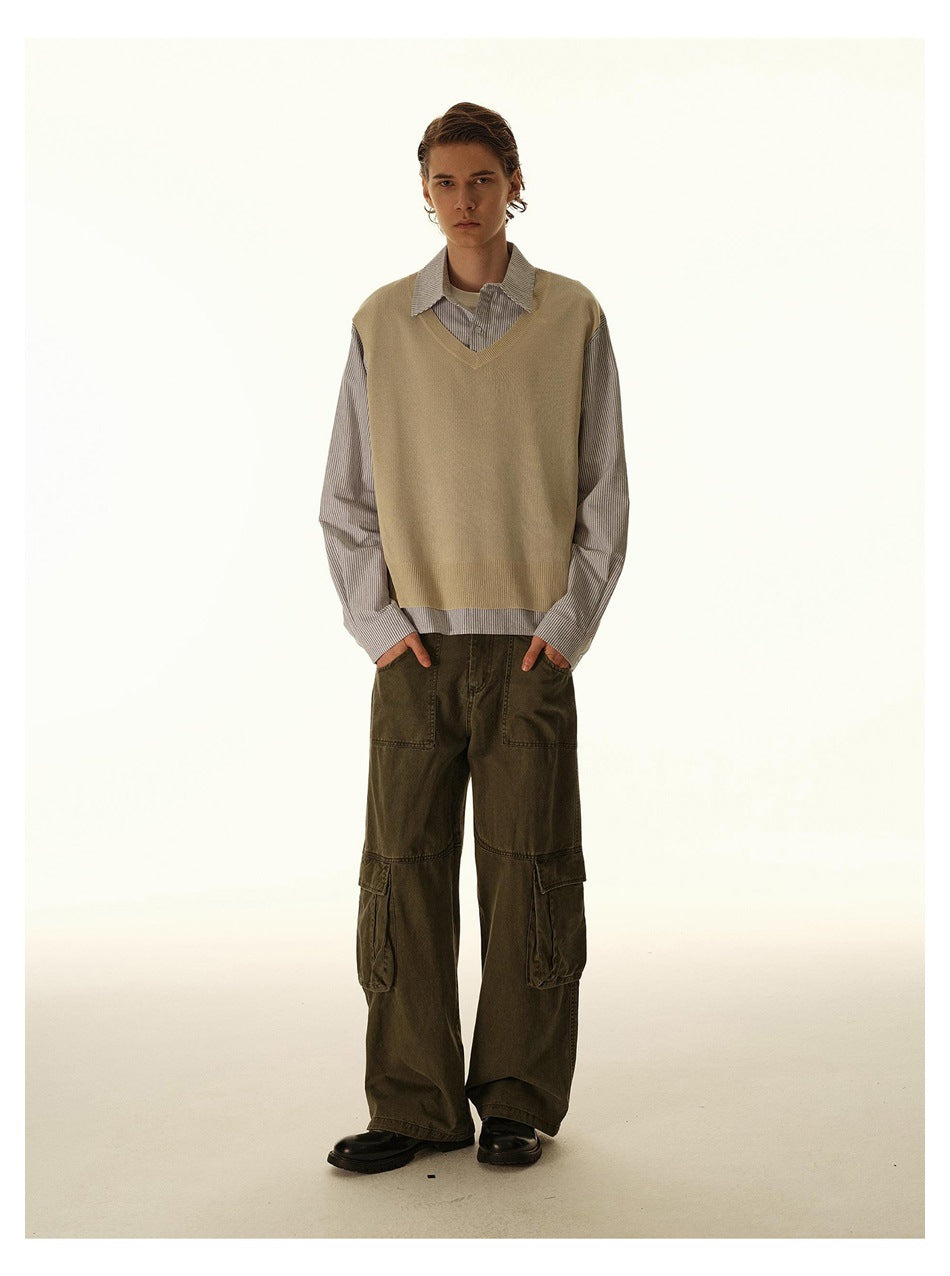 Full-length male model wearing a beige V-neck vest over a fine-striped shirt and olive cargo pants.
