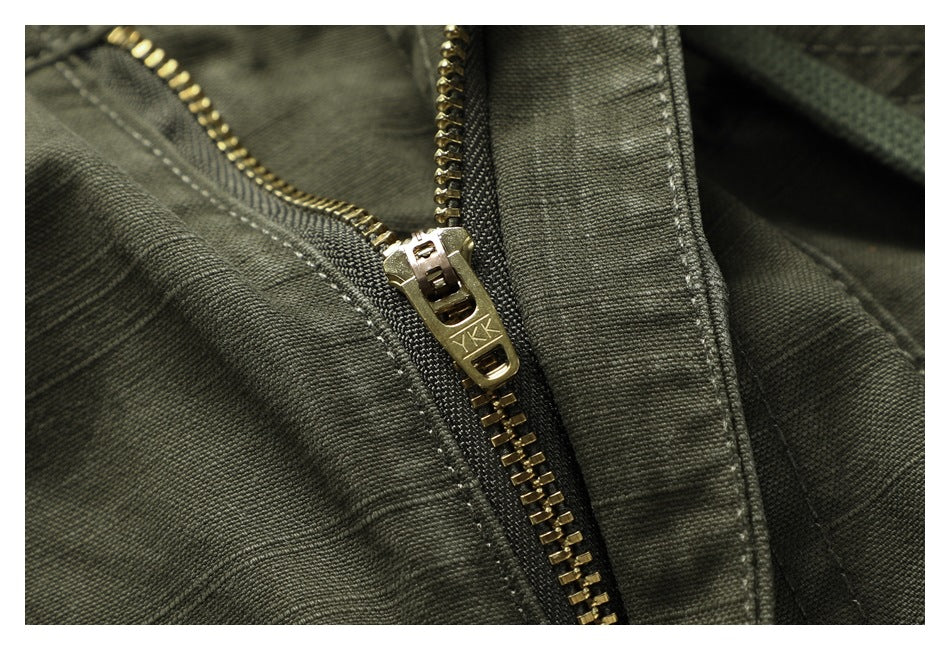 Macro view of a brass-colored zipper marked YKK on olive-green pants.