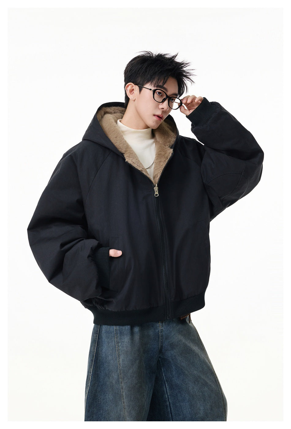Man wearing a black hooded zip jacket with a plush tan lining and ribbed cuffs, styled with wide-leg jeans