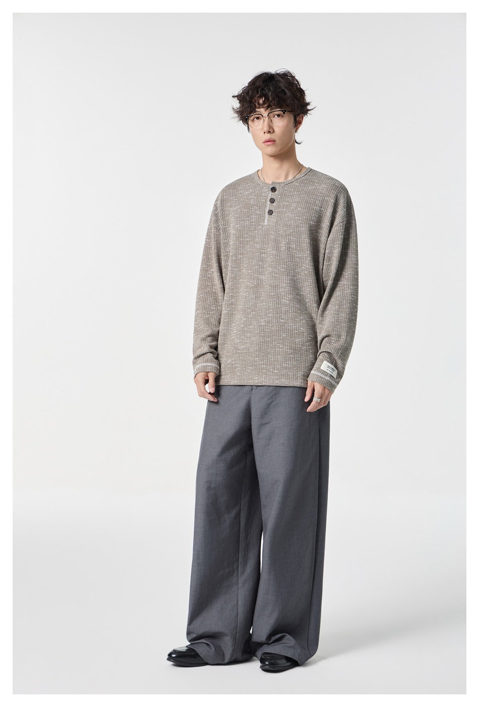 Model wearing a taupe marled long-sleeve Henley shirt with a three-button neckline and dark wide-leg trousers.