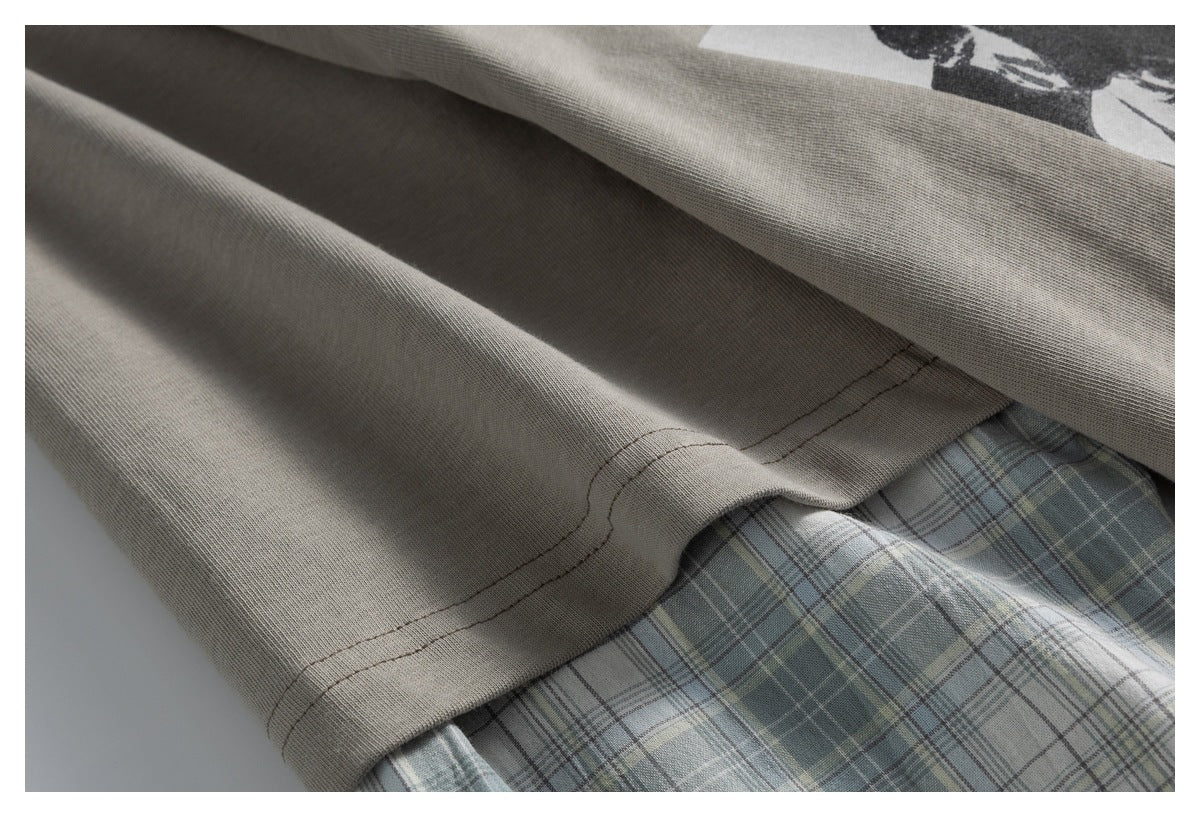 Close-up of the taupe T-shirt hem and stitching layered over pale blue-gray plaid fabric.