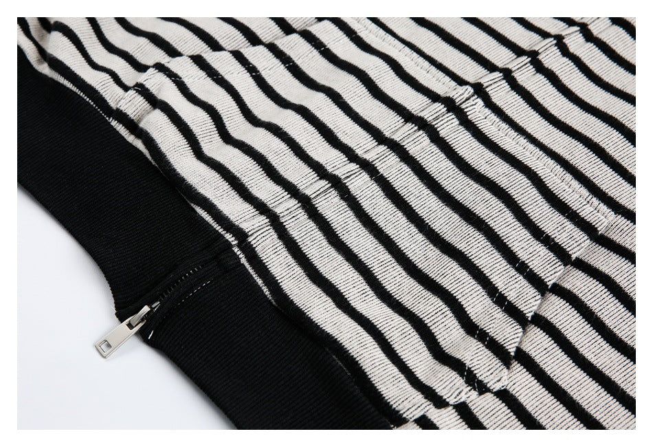 Close-up of a silver zipper beside a black ribbed band and a seam on black-and-white striped knit fabric.