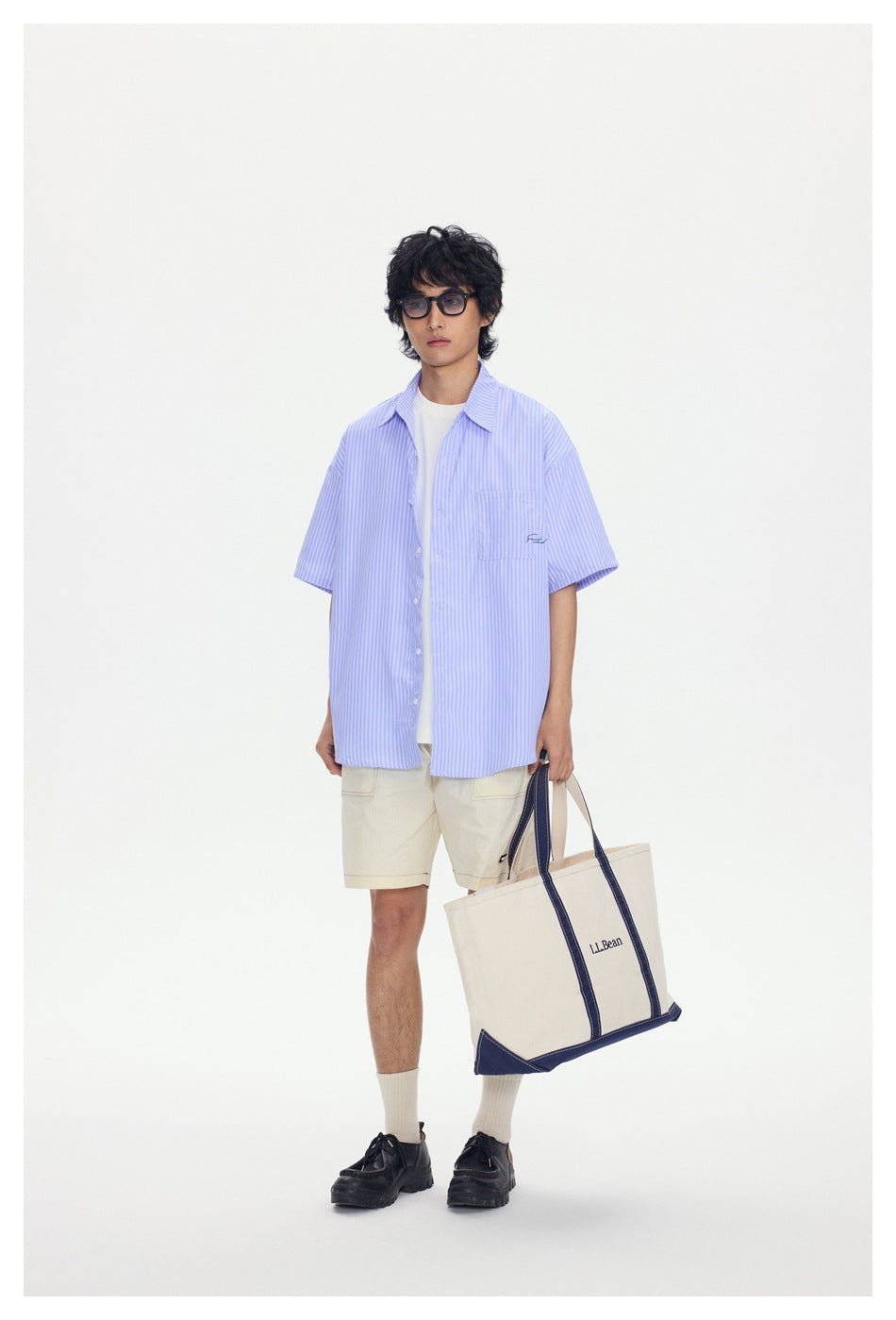Model wearing an oversized light blue-and-white striped short-sleeve shirt over a white tee, with cream shorts.