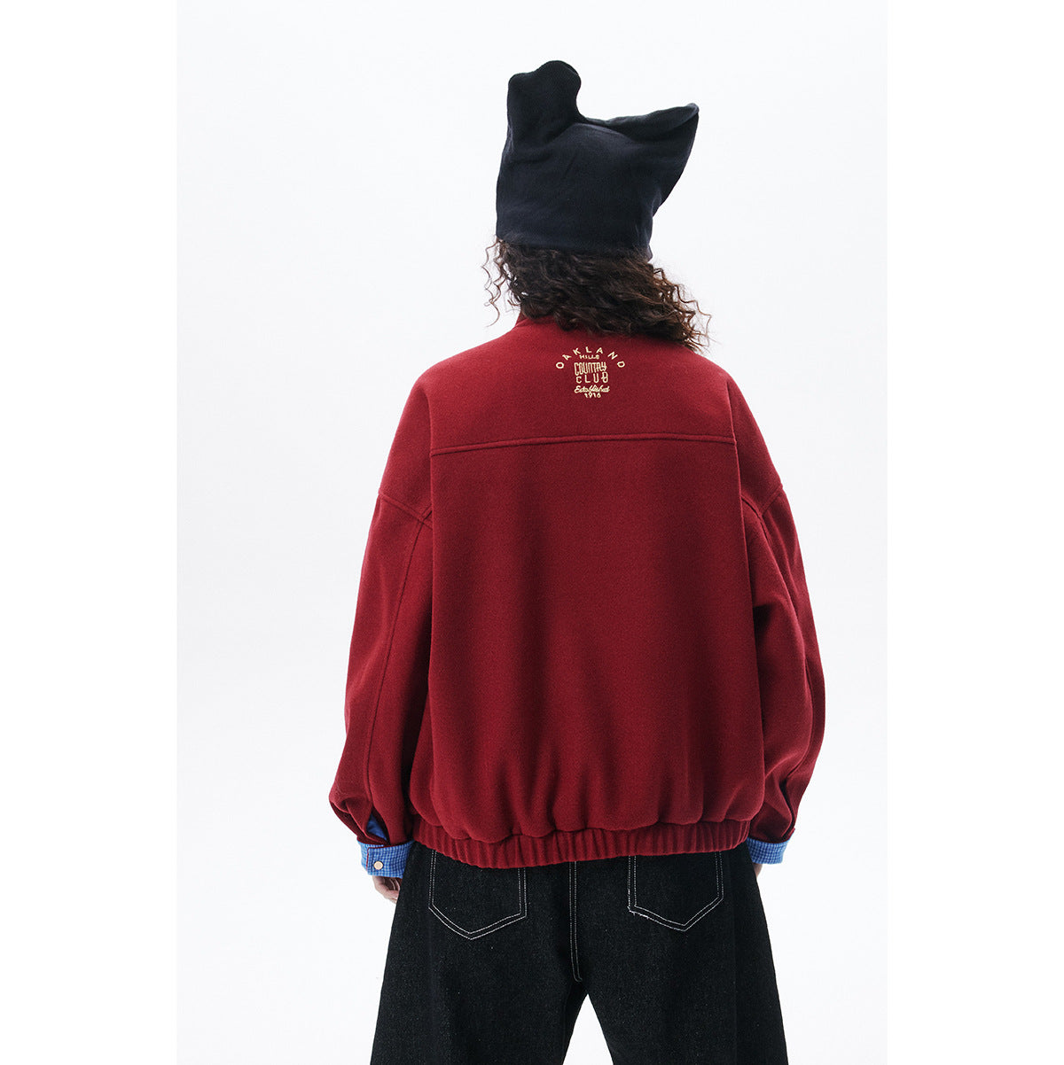 Rear view of a model wearing a burgundy jacket with a small embroidered design across the upper back.
