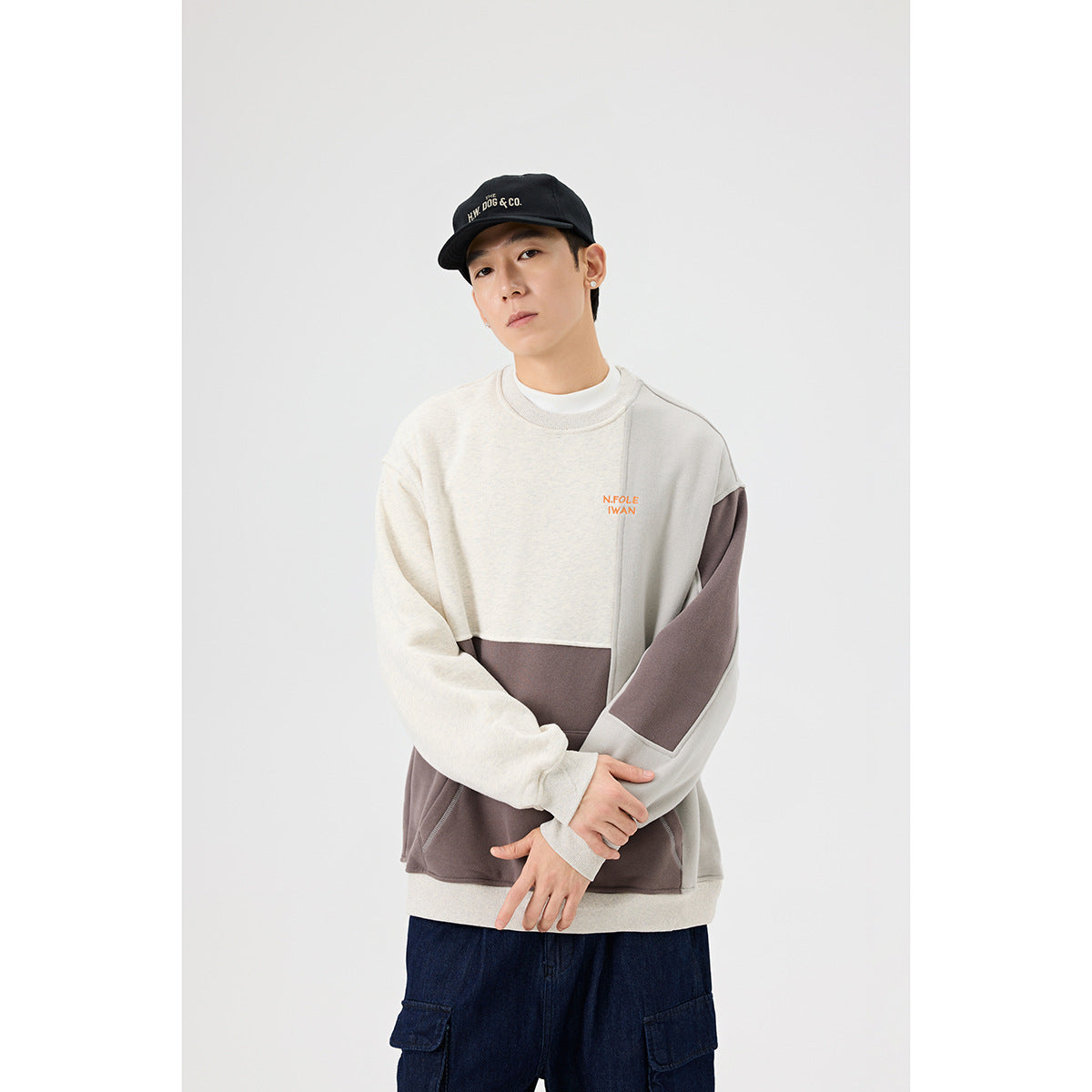 Model wearing a cream, light gray, and taupe color-block crewneck sweatshirt with a front pocket.