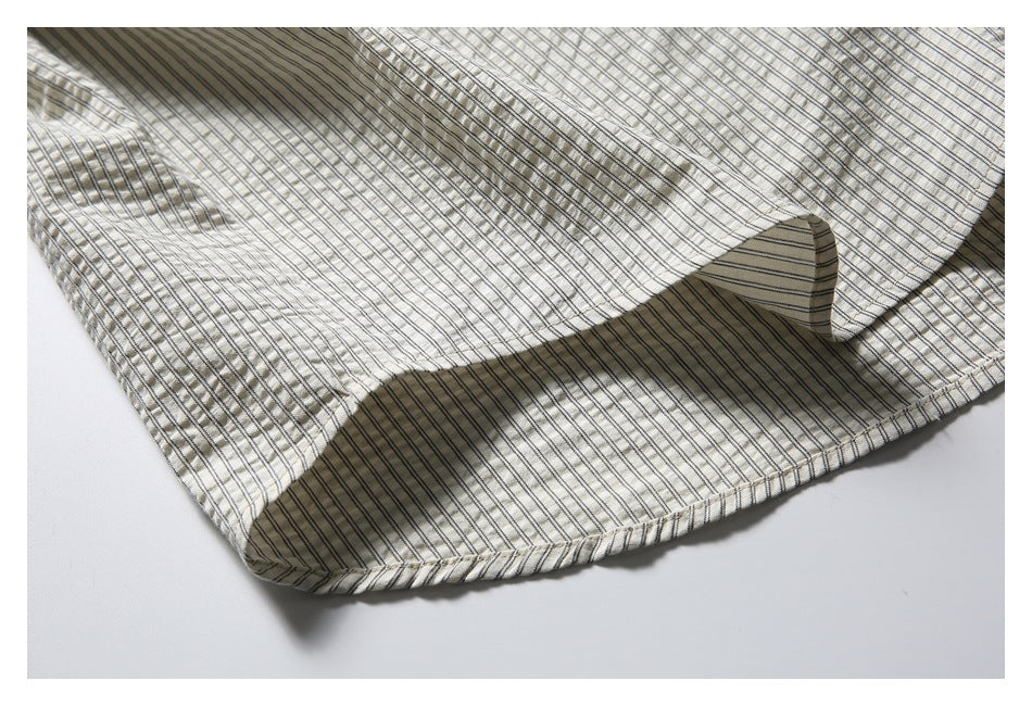Close-up of a cream garment hem with narrow dark pinstripes and visible stitching.