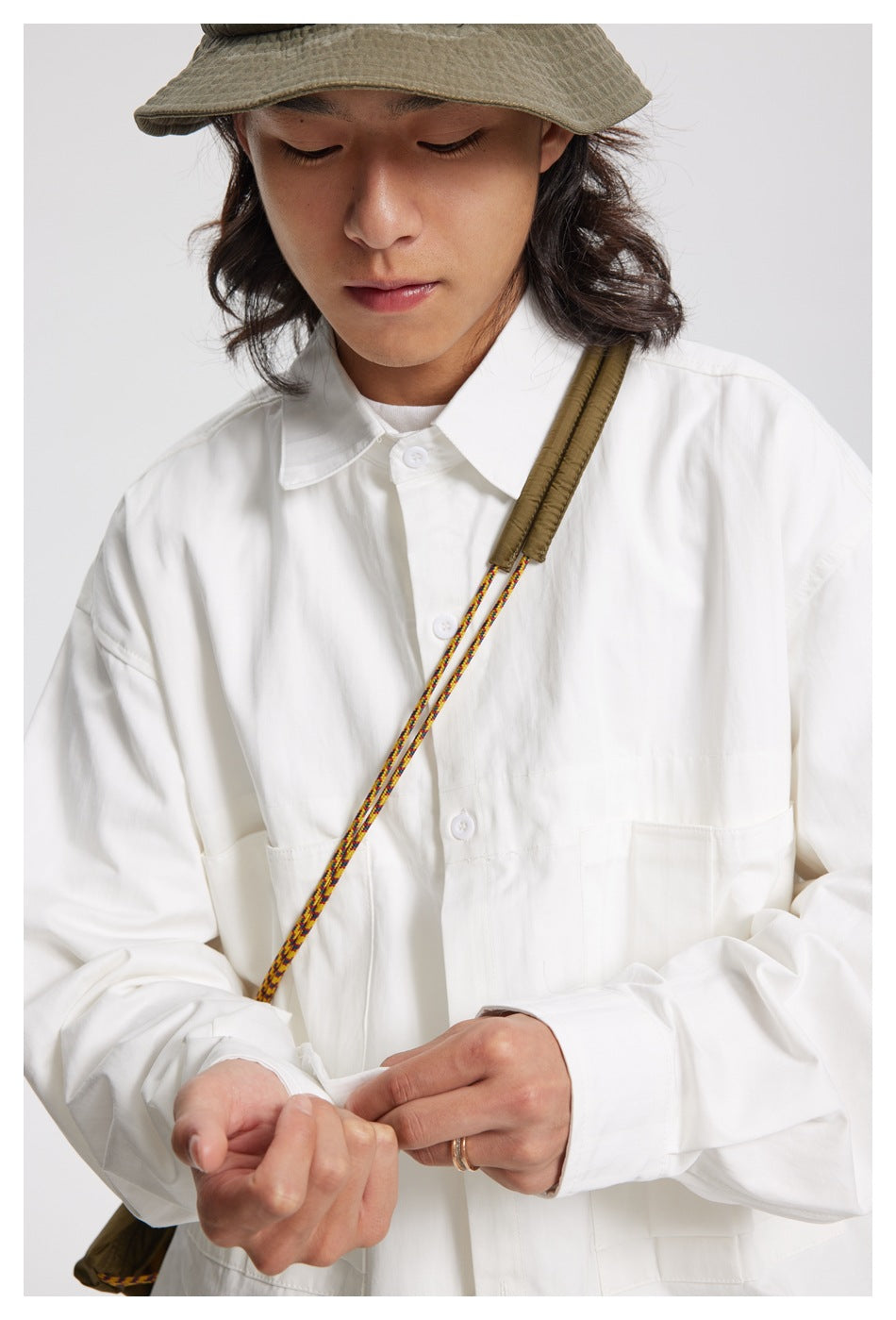 Close-up of a model wearing a white button-up shirt and a colorful shoulder cord.