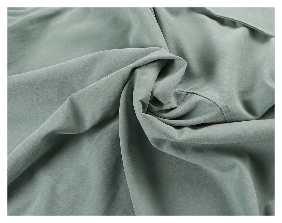 Close-up of draped sage green garment fabric showing folds and stitched seams.