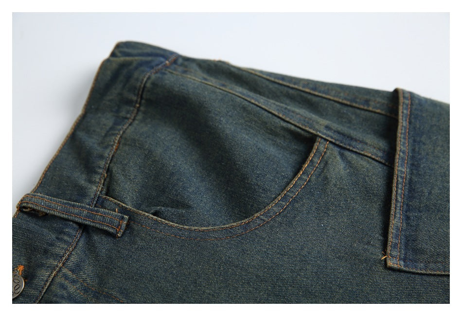 Close-up of dark blue jeans showing a curved front pocket, waistband, belt loop, and orange topstitching.