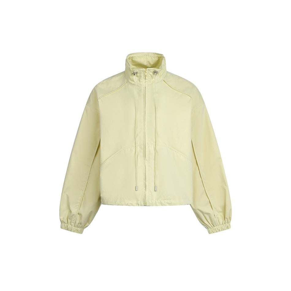 Light yellow cropped zip jacket with stand collar, drawstring cords, curved front seams and elastic cuffs on white background
