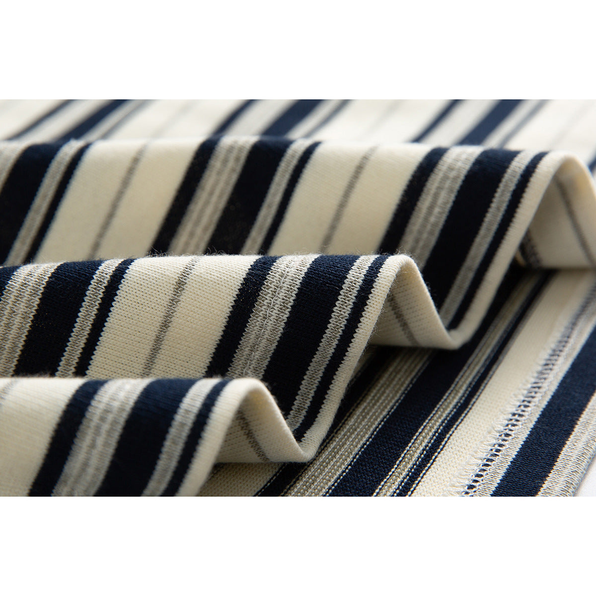 Close-up of folded cream knit fabric with alternating navy, gray, and fine striped bands.
