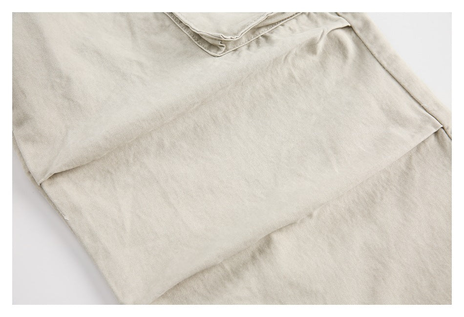 Close-up of light beige trouser fabric with the edge of a flap pocket and seam stitching.