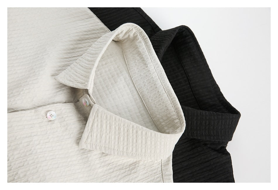 Close-up of ivory and black textured collared shirts, showing their pointed collars and iridescent buttons.