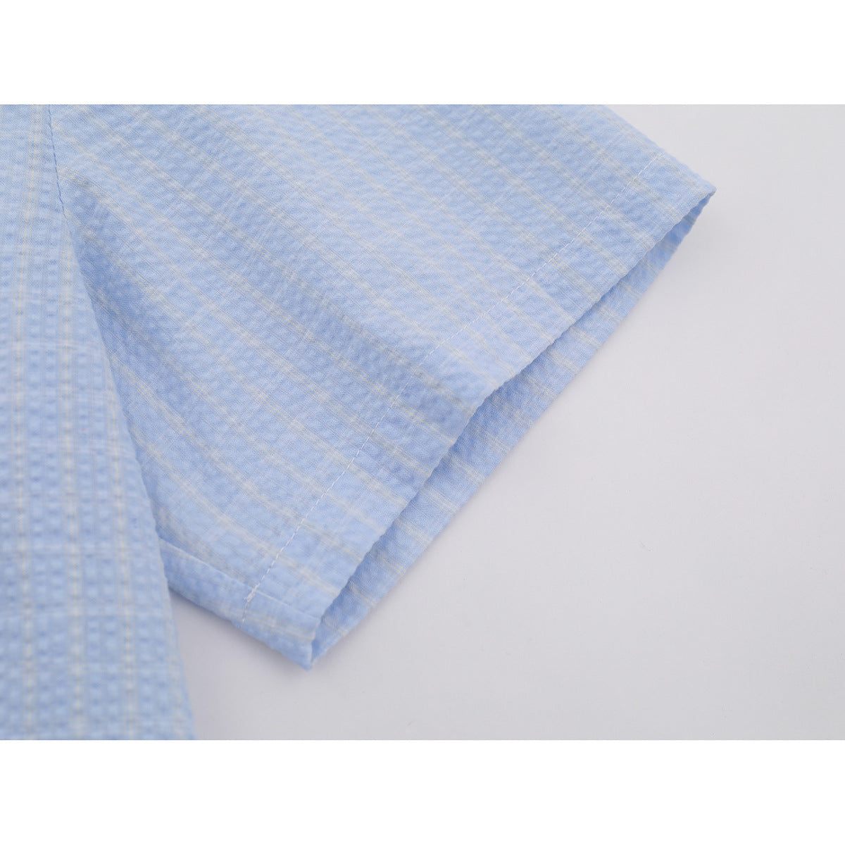 Close-up of a light blue short sleeve and stitched hem, showing a subtle plaid pattern.
