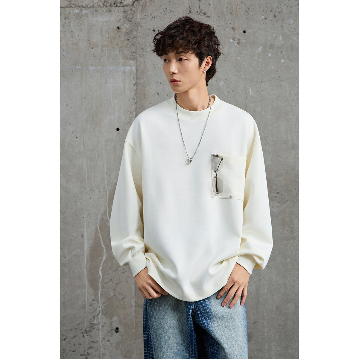 Close view of a model wearing a white oversized crewneck sweatshirt with a chest pocket holding sunglasses.