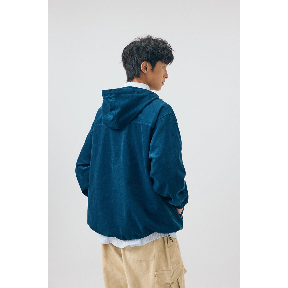 Rear view of a model wearing a navy hooded pullover with an adjustable hem and beige cargo pants.