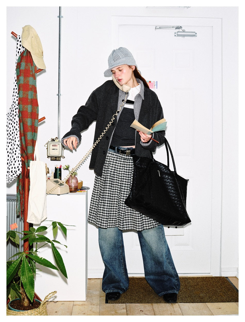 Model wears a charcoal button-front jacket over a dark top, a gingham skirt layered over wide-leg jeans, and a gray knit hat.