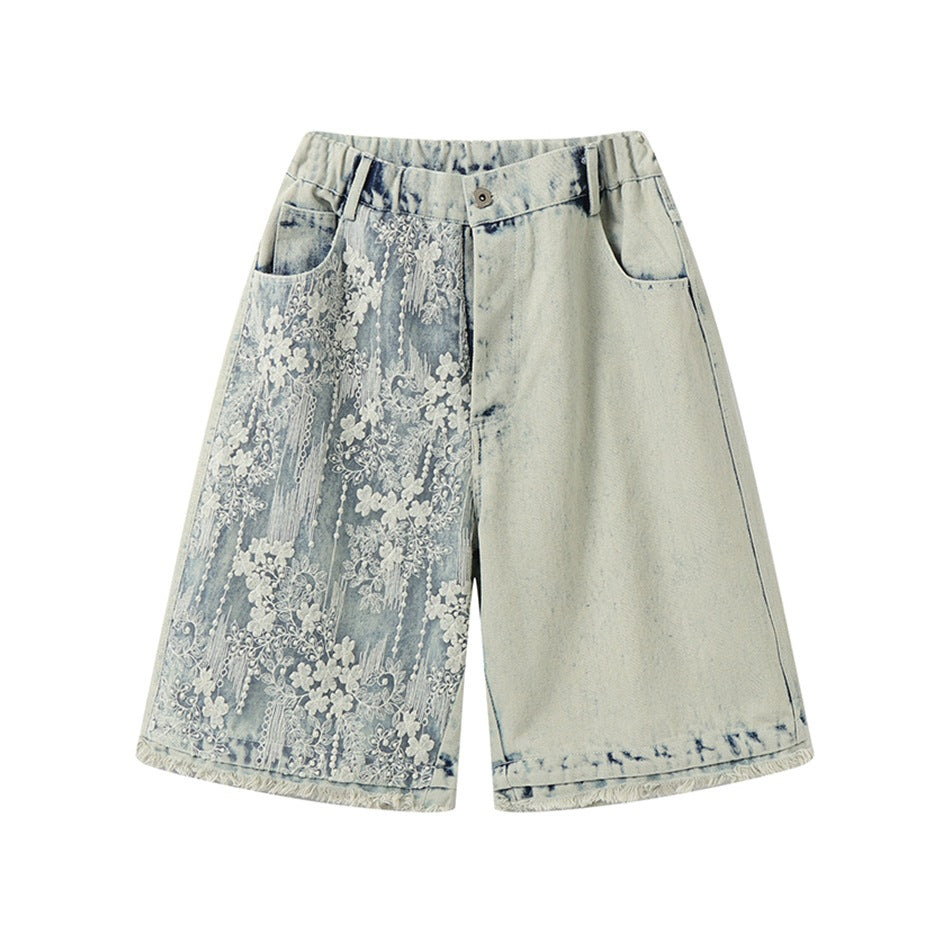 Light blue washed denim shorts with white floral lace panel on the left leg, front view on a white background