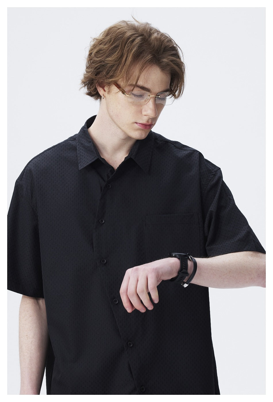 Model wearing a black short-sleeve button-up shirt with a subtle texture and a chest pocket, shown close up.
